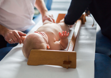 Infant being measured for length with an infantometer by two health care providers