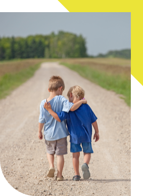 Two children, seen from behind, walking down a dirt road with arms around each other