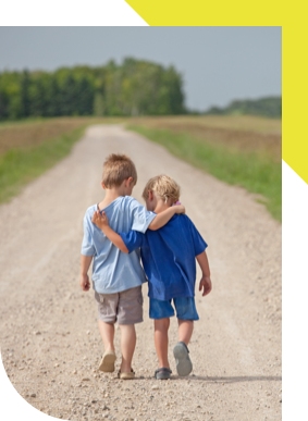 Two children, seen from behind, walking down a dirt road with arms around each other